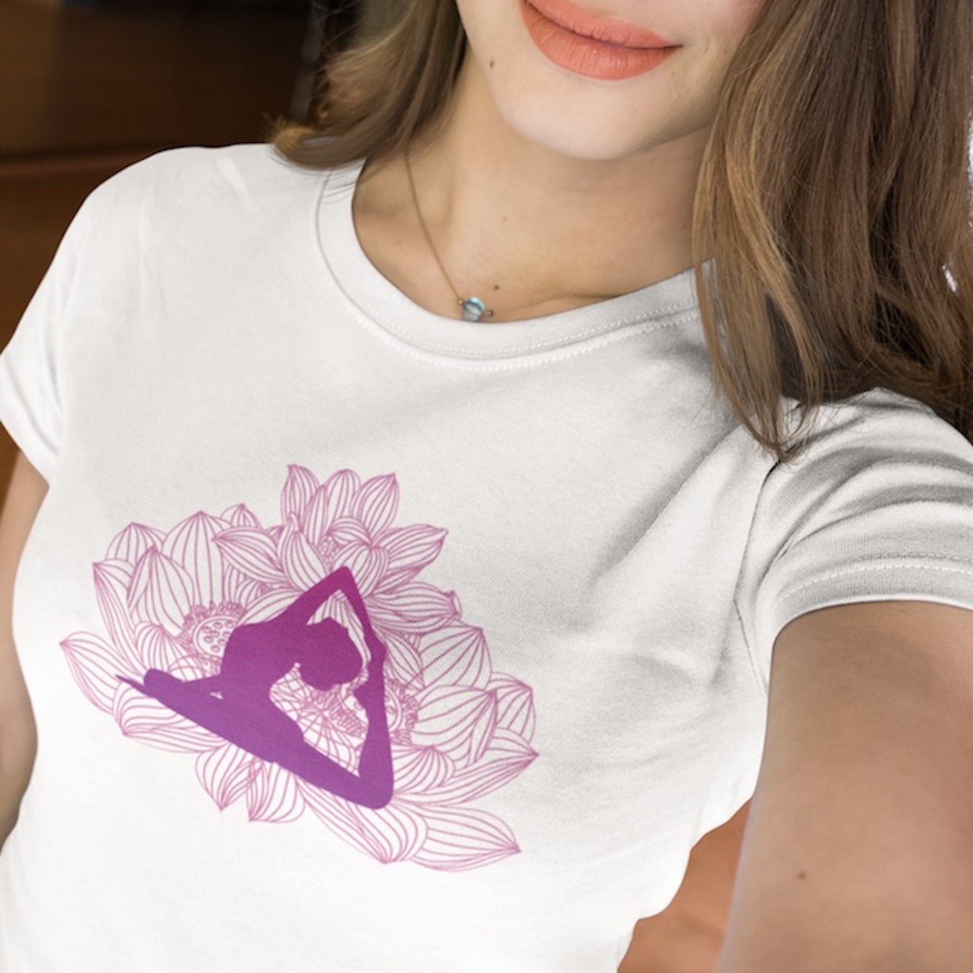 Une femme portant un tee-shirt blanc avec un motif de lotus rose et une silhouette en position de yoga, accessoirisé d’un collier délicat, pour HappyAndShiny.com.