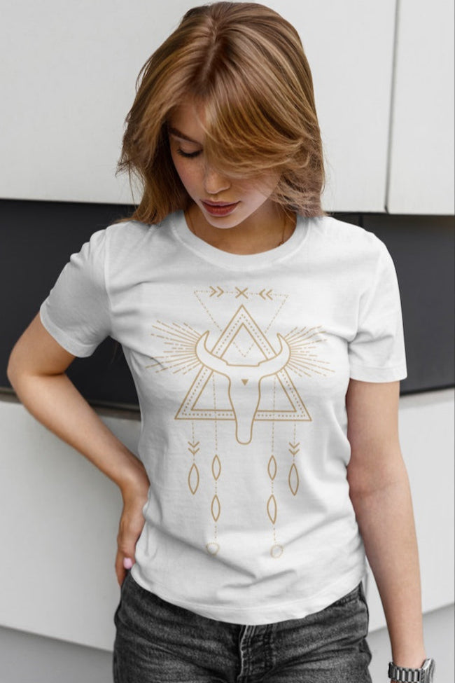 Design de Happy and Shiny sur un t-shirt blanc, représentant un crâne de taureau doré à l'intérieur d'un triangle géométrique, surmonté de rayons