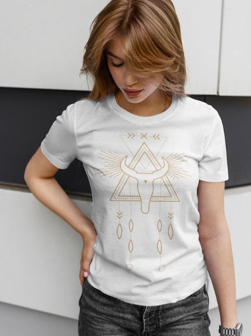 Une femme portant un tee-shirt blanc avec un motif géométrique de crâne de taureau orné de plumes, devant un fond minimaliste blanc et noir, pour HappyAndShiny.com.