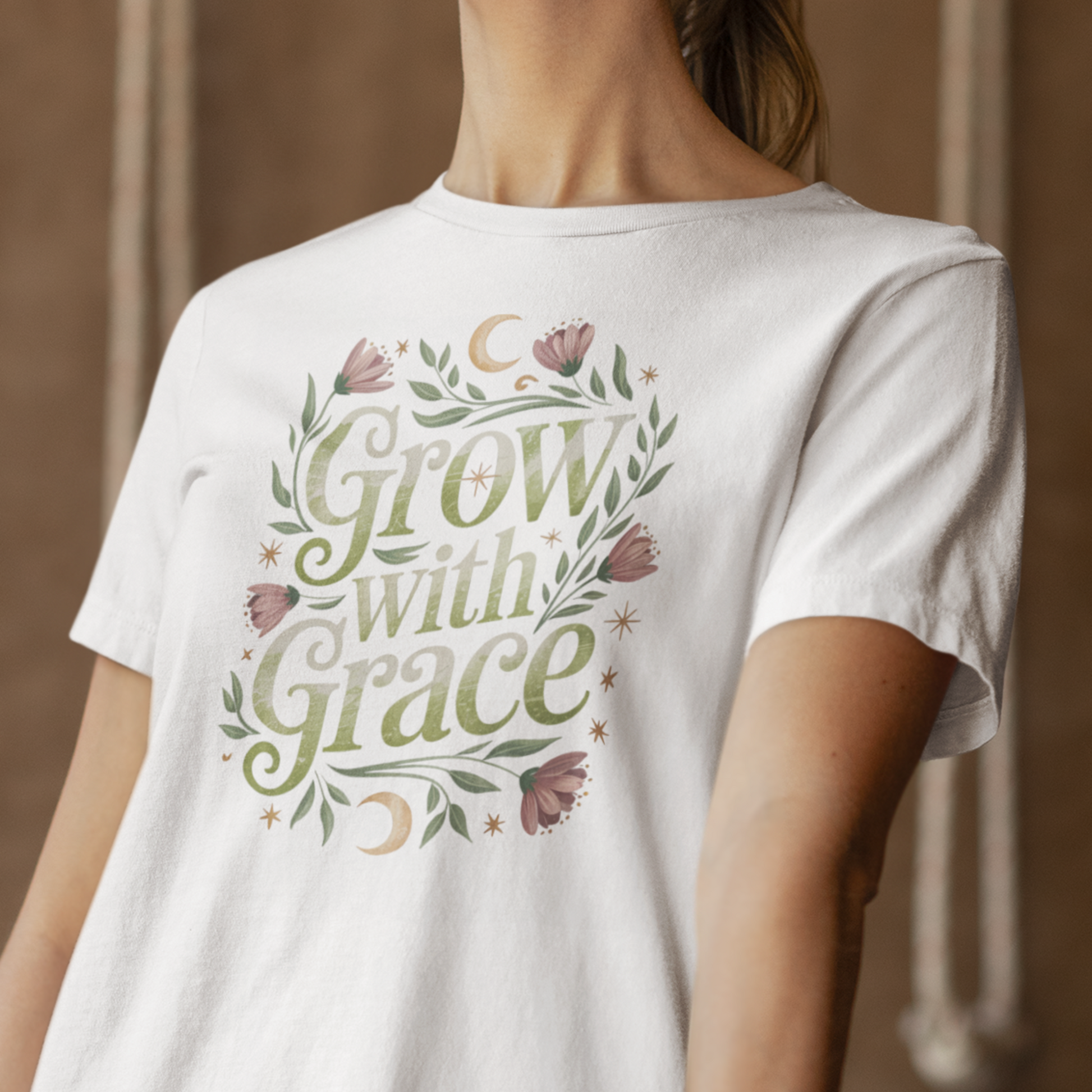 Une femme portant un tee-shirt blanc avec l’inscription "Grow With Grace" entourée de motifs floraux et de lunes, devant un fond beige texturé, pour HappyAndShiny.com.