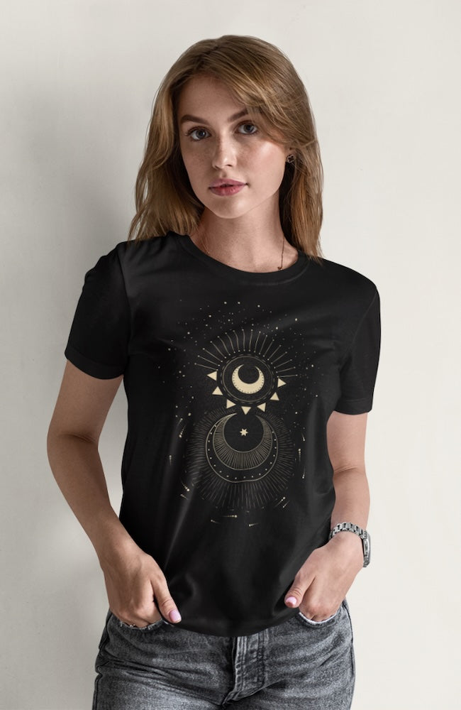 Une femme portant un tee-shirt noir avec un motif céleste de lunes et d’étoiles, associé à un jean gris, dans un décor minimaliste blanc, pour HappyAndShiny.com.