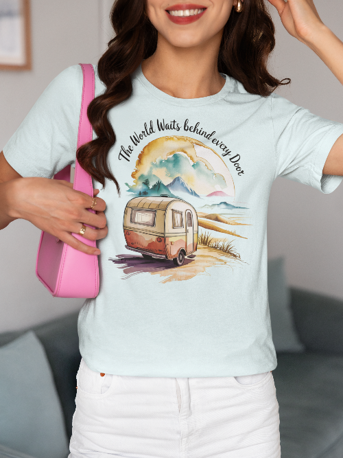 Femme souriante portant un t-shirt clair avec une caravane et l'inscription 'The World Waits beyond every Door', tenant un sac rose vif, dans un intérieur avec canapé