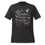 T-shirt unisexe avec un design apaisant affichant le texte "Breathe, Trust, Let Go" (lettres blanches) entouré d’oiseaux, plumes et motifs célestes (lunes, étoiles) en teintes pastel.