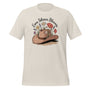T-shirt unisexe beige avec un design bohème d’un chapeau de cowboy rempli de fleurs (lavandes, coquelicots, marguerites) et le texte "Even Silence Blooms".