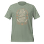 T-shirt unisexe avec un design spirituel affichant le texte "Let Your Light Guide You" (lettres blanches) entouré de motifs bohèmes (soleils, lunes, étoiles, plumes) beige et orangés.