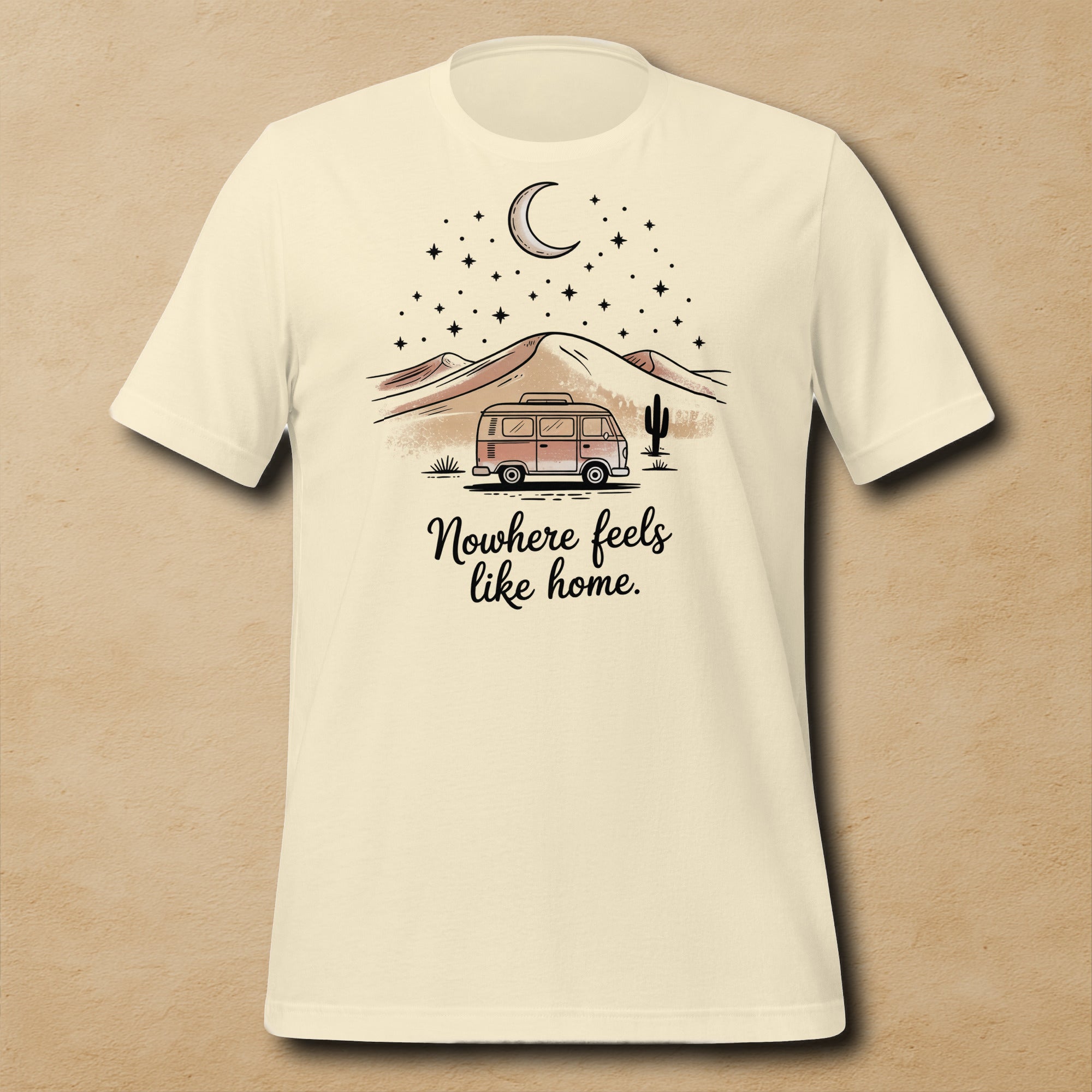 T-shirt unisexe beige avec un design bohème d’un van vintage, un paysage désertique, une lune croissante, des étoiles et le texte "Nowhere feels like home".