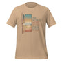 T-shirt unisexe beige avec un design bohème d’une porte ouverte sur un paysage désertique, des montagnes, un ciel étoilé et le texte "The world waits behind every door".