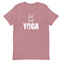 T-shirt rose poudré unisexe avec un design bohème affichant le texte "But first YOGA" en blanc, accompagné d’une silhouette méditative en position de lotus intégrée dans la lettre "O"