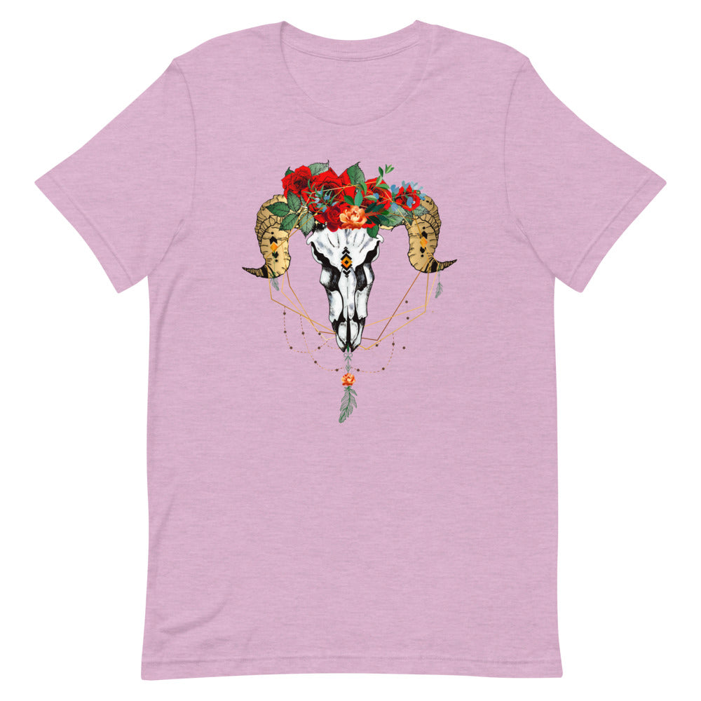 T-shirt rose pâle unisexe avec un design bohème d’un crâne de bélier blanc et noir orné de fleurs rouges, roses et blanches, intégré dans un capteur de rêves doré avec plumes et perles.