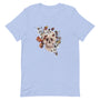 T-shirt unisexe bleu pâle avec un design bohème d’un crâne humain orné de fleurs automnales (blanches, orange, roses), feuillages et détails naturels, style spirituel.