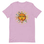 T-shirt rose pâle unisexe avec un design bohème d’un soleil orange entouré de rayons dorés et de fleurs multicolores roses, bleues, blanches et jaunes, dans un cercle doré.